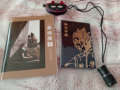 美術展ハンドブック、御朱印帳（婆娑羅の表紙）、単眼鏡、ネコの飾り物の画像